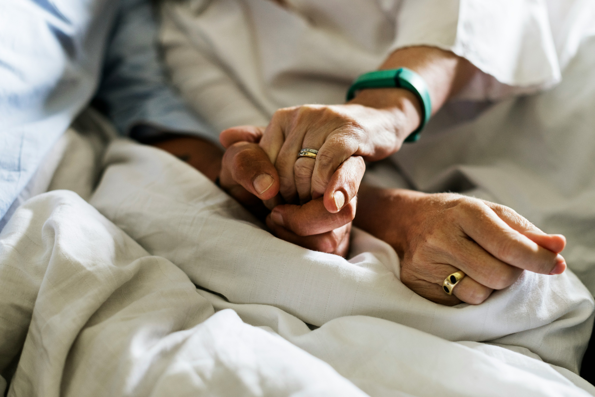 In-home Reiki support in San Diego — two pairs of hands held gently in soft bedside light