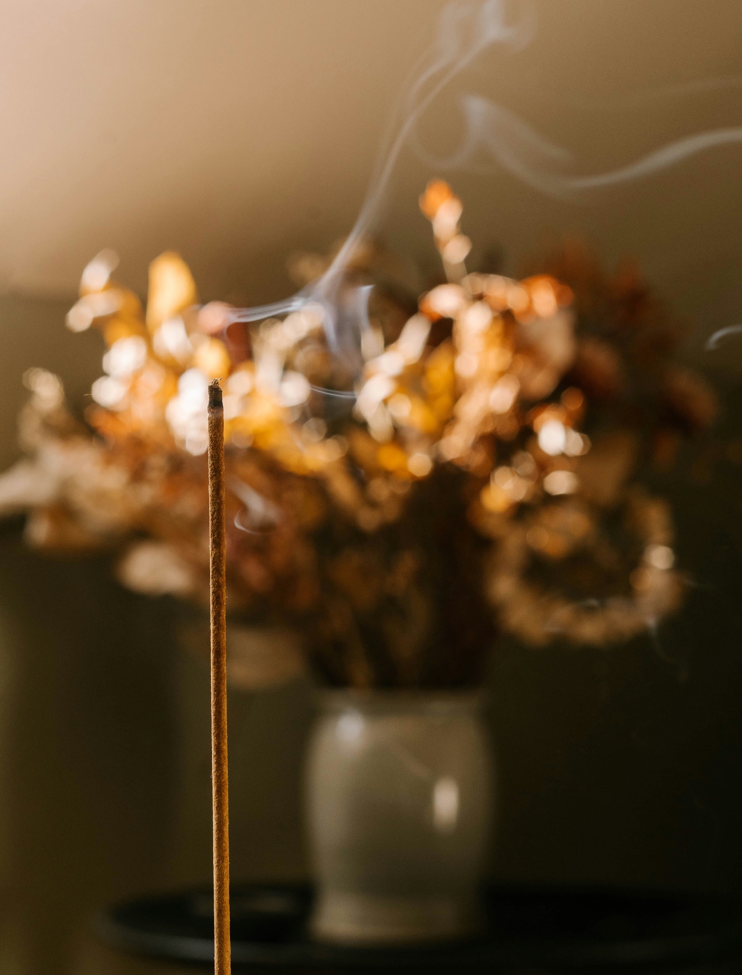 A single incense stick with soft smoke rising near dried florals