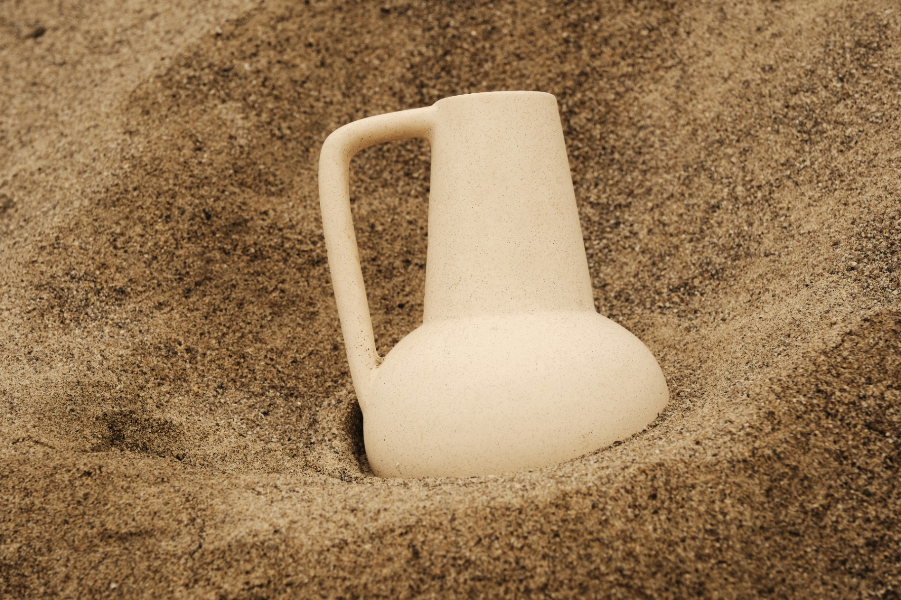 A delicate ceramic vessel resting in soft sand — a quiet symbol of presence and containment